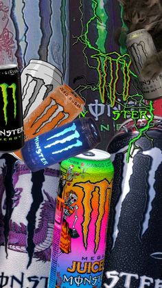 two cans of monster energy drink and a can of juice on a bed covered with wallpaper