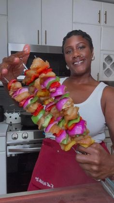 a woman holding a skewer of food in her hand while standing next to an oven