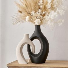 two black and white vases with dried flowers in them sitting on a wooden shelf