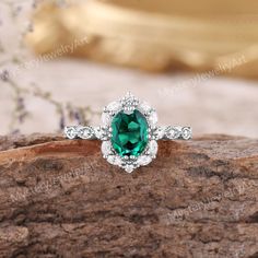 an oval cut green and white diamond ring on top of a tree branch with flowers in the background