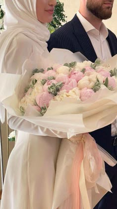 a man and woman dressed in wedding attire hold a bouquet of flowers while standing next to each other