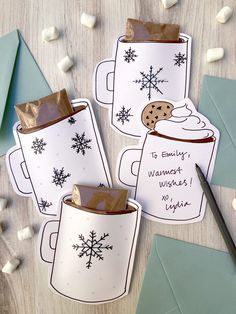 three coffee mugs with snowflakes on them are sitting next to some envelopes