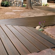 a wooden deck in front of a tree with rocks and gravel around it on the ground