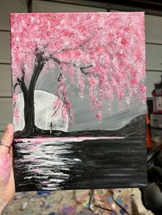 a person holding up a piece of art that looks like a tree with pink flowers