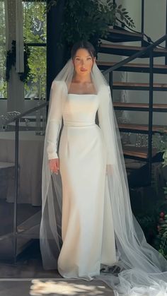 a woman in a white wedding dress and veil standing next to a staircase with greenery