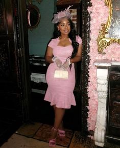 a woman in a pink dress and hat standing next to a wall with flowers on it