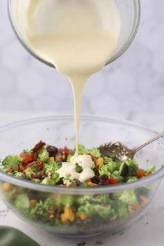 dressing being poured over a salad in a glass bowl