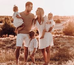 a man, woman and two children are standing in the grass with their arms around each other