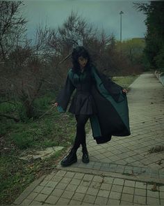 a woman walking down a sidewalk wearing a black and green coat with long sleeves on