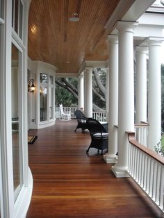 the porch is lined with white pillars and black chairs on it's wooden floor