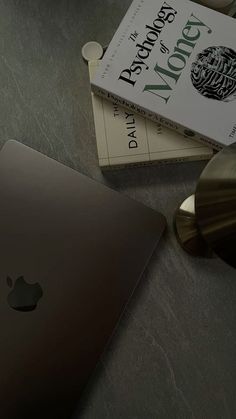 an apple laptop computer sitting on top of a table next to a book and lamp