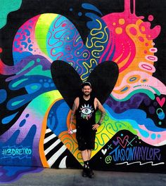 a man standing in front of a colorful wall with a heart on it's chest