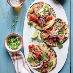 three tacos on a plate with onions, cilantro and lime wedges