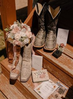 boots and flowers are sitting on a wooden bench next to wedding cards, notepads, and other items