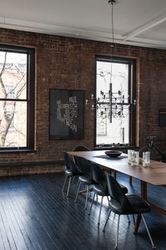 an empty dining room with wooden floors and brick walls is pictured in this image, there are two windows that look out onto the trees outside