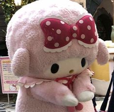 a pink hello kitty stuffed animal with a red bow on its head and neck, standing in front of a woman's purse