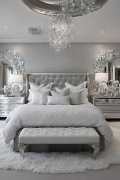 a white bed sitting under a chandelier next to a mirror covered dresser and chair