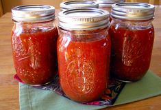 four jars filled with red sauce sitting on top of a table