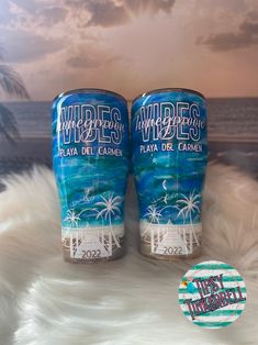 two cans of wine sitting on top of a white fur covered floor next to the ocean