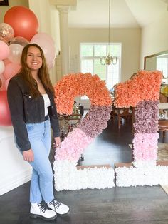 a woman standing in front of a large letter made out of flowers with balloons behind her