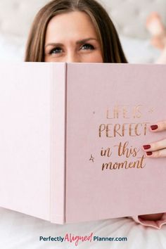 a woman laying in bed reading a book with her hand on top of the book that says life is perfect in this moment