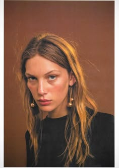 a woman with long blonde hair wearing gold earrings and black shirt looking at the camera