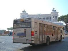 a bus is driving down the street in front of a building with statues on it