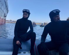 two people sitting on a boat in the water wearing scuba suits and goggles,