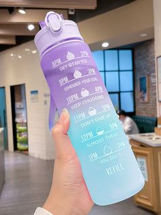 a person holding up a purple and blue water bottle in an office building with people working behind them