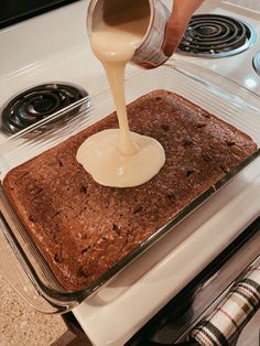 someone pouring batter on top of a cake in a glass baking dish over an oven