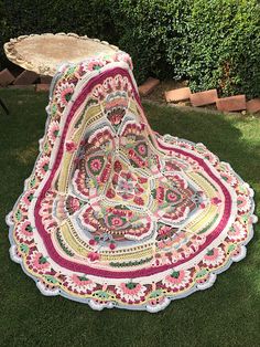 a crocheted tablecloth is sitting on the grass in front of some bushes