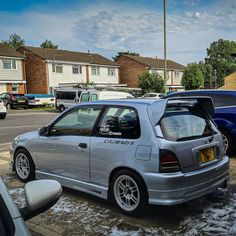 a silver car parked on the side of a road next to other cars and houses