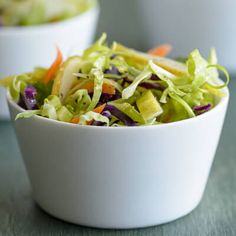 a white bowl filled with lettuce and carrots on top of a table