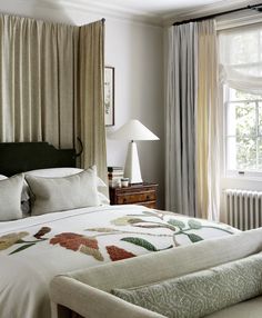 a large bed sitting next to a window in a room with curtains on the windowsill