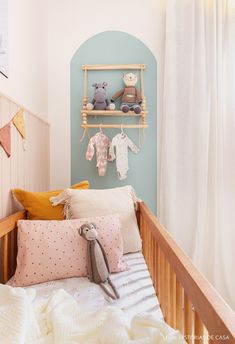 a baby's crib with stuffed animals and clothes hanging on the wall next to it