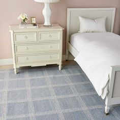 a white bed sitting next to a dresser with a lamp on top of it