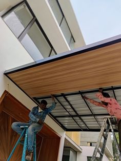 two men on ladders are painting the roof of a building with wood panels and metal bars