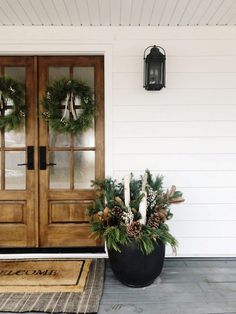 two christmas wreaths on the front door of a white house with wooden double doors