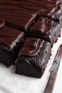 a chocolate cake is cut into squares and ready to be eaten with a knife next to it