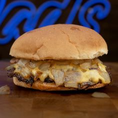 a cheeseburger sitting on top of a wooden table next to a neon sign