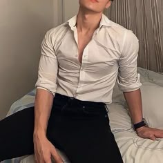 a man sitting on top of a bed wearing black pants and a white button up shirt