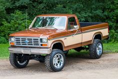 a brown truck parked on top of a dirt road next to green grass and trees