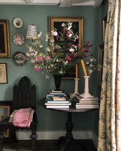 a table with flowers and books on it next to a chair in front of a window