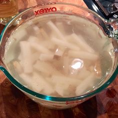 a glass bowl filled with white food on top of a wooden table next to two glasses