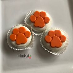 three cupcakes with white frosting and orange paw prints on them are sitting on a plate