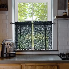 a kitchen window with black lace curtains in front of an open stove top and coffee maker on the counter