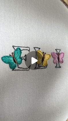 three embroidered butterflies sitting on top of a white piece of cloth with a video playing in the middle