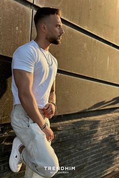 man leaning on the wall wearing the white t-shirt, linen pants, white tshirt, chain necklace, beaded bracelets. The Holy Trinity, Bracelets And Rings, The Right Man, Holy Trinity, Summer Accessories