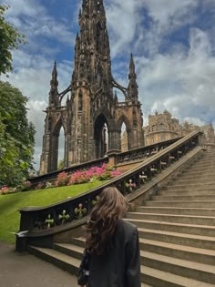 a woman is walking up some stairs towards a castle like building with flowers in the foreground