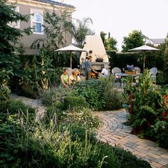 people sitting at tables in a garden with lots of greenery and plants on the ground